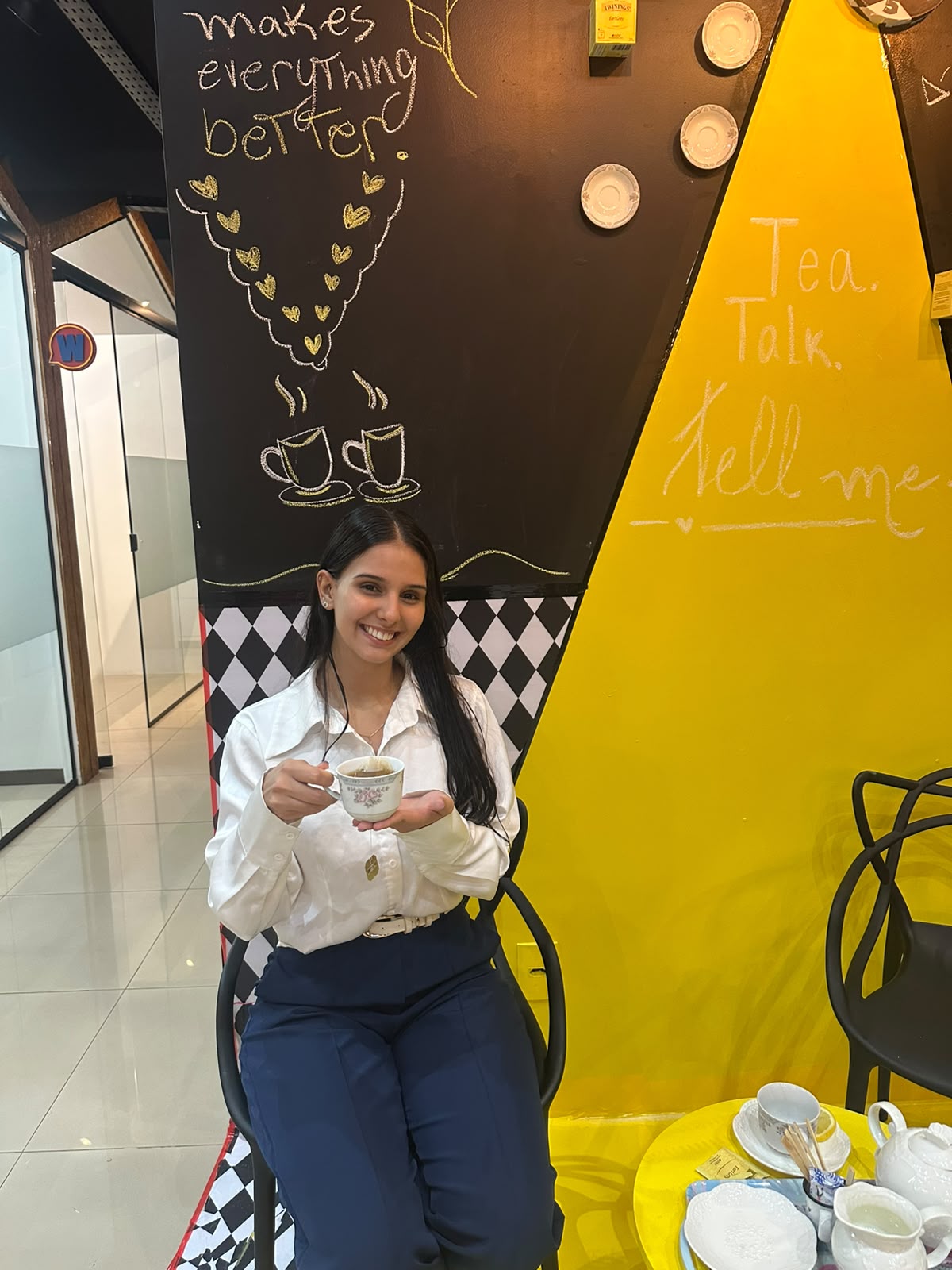 Aluna sorrindo com xícara de chá em frente ao painel do English Tea