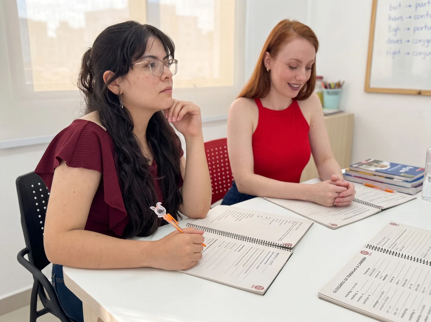 Duas alunas adultas estudando inglês na Tell Me com cadernos de atividades abertos sobre a mesa