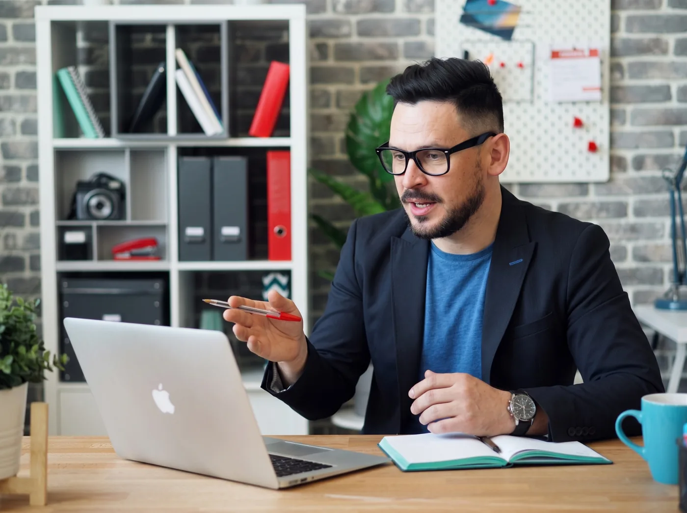 Profissional de óculos e blazer falando em inglês durante uma videochamada de trabalho no notebook